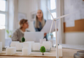 Women eco architects working together in office, with a wind turbine in foreground.